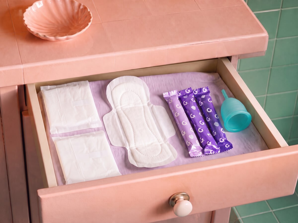 A bathroom drawer holding wrapped Garnuu pads, an open winged pad, tampons and a cup
